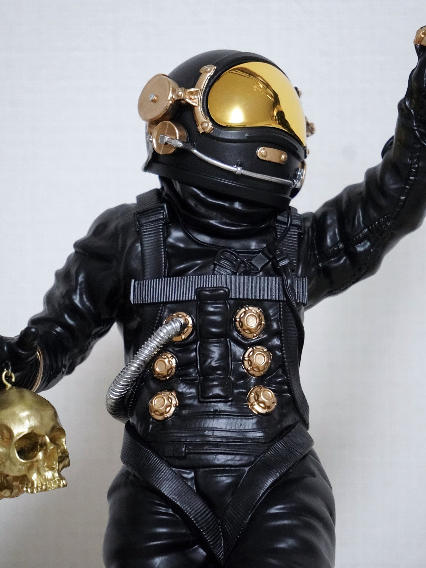 Black and gold astronaut figure with helmet and suit holding a skull against a white background. Jeremy geddes